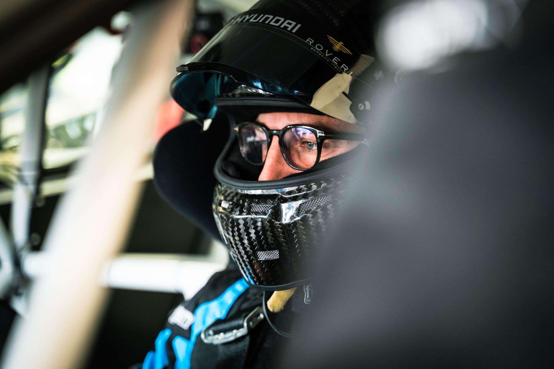 Pilote portant un casque et des lunettes assis dans l’habitacle d’une voiture de course.
