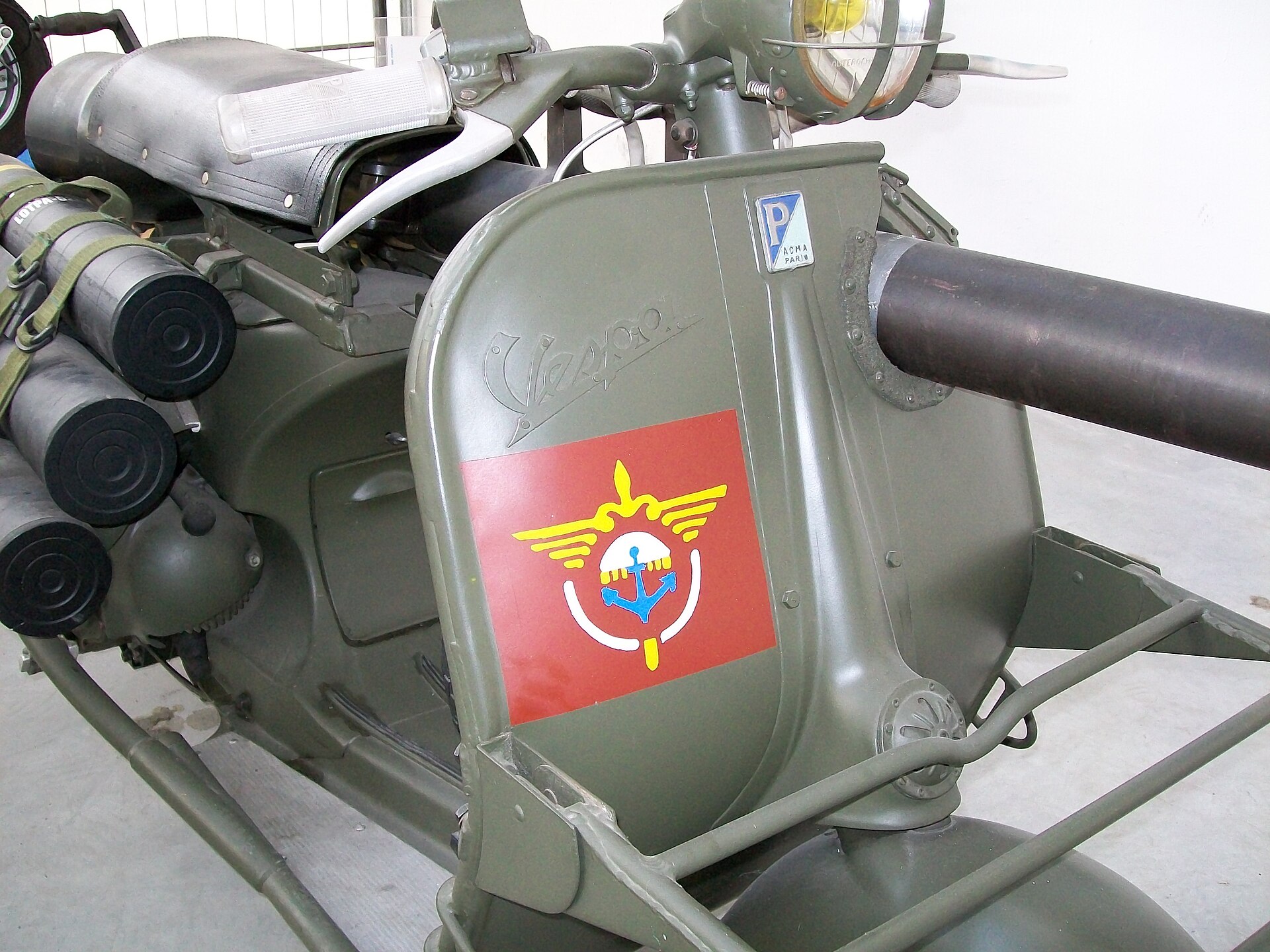 Tablier vert olive d’une Vespa Tap militaire avec insigne rouge, phare grillagé et tube de canon